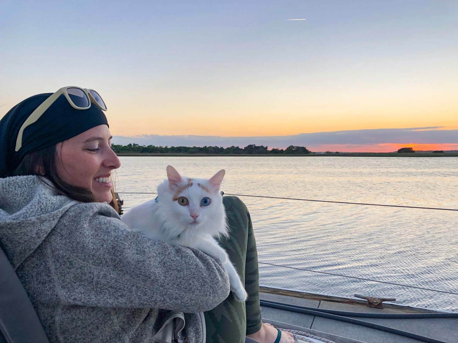 woman sitting on boat holding cat and watching the sunset