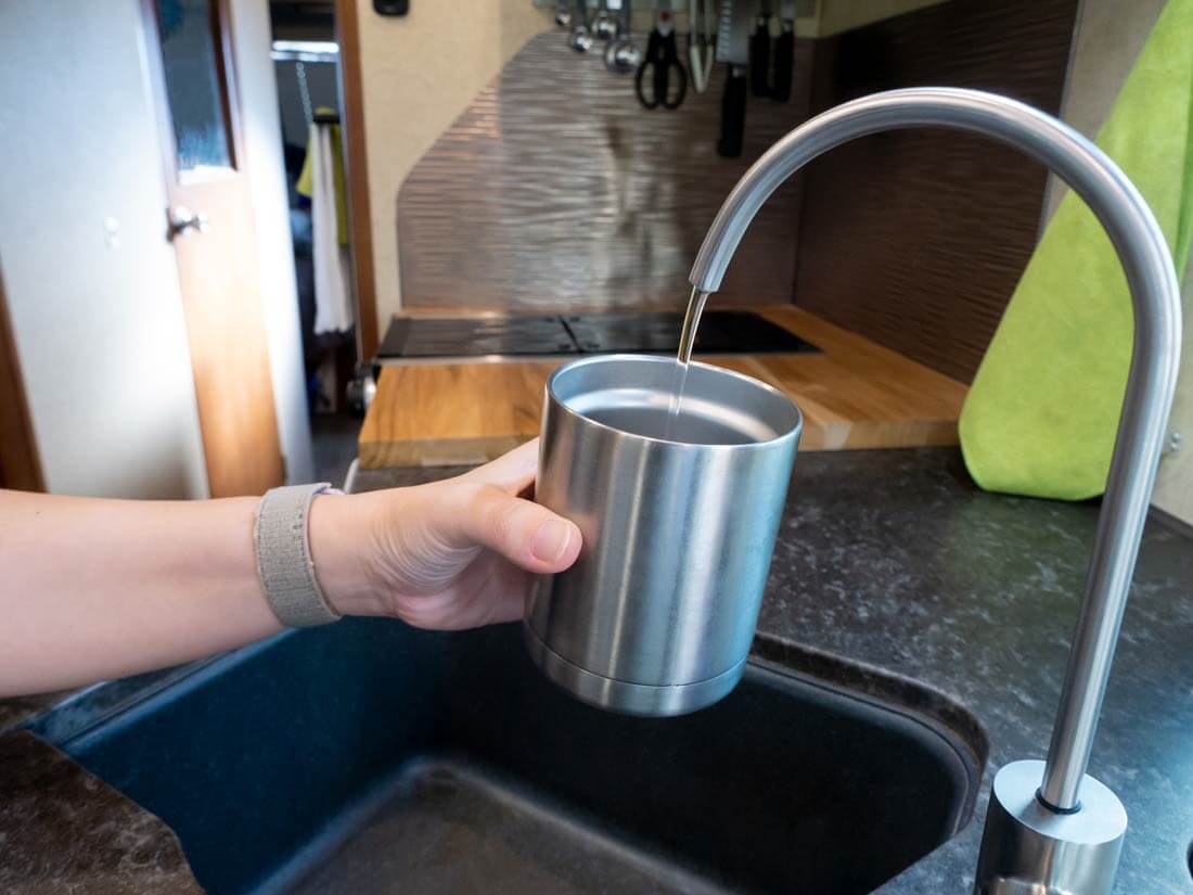 Water purifying faucet with water running into a stainless steel cup.