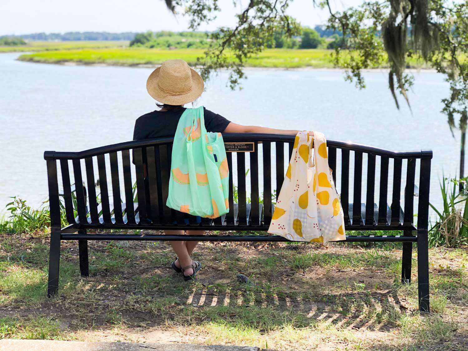 woman sitting beside waterfront holding reusable bags