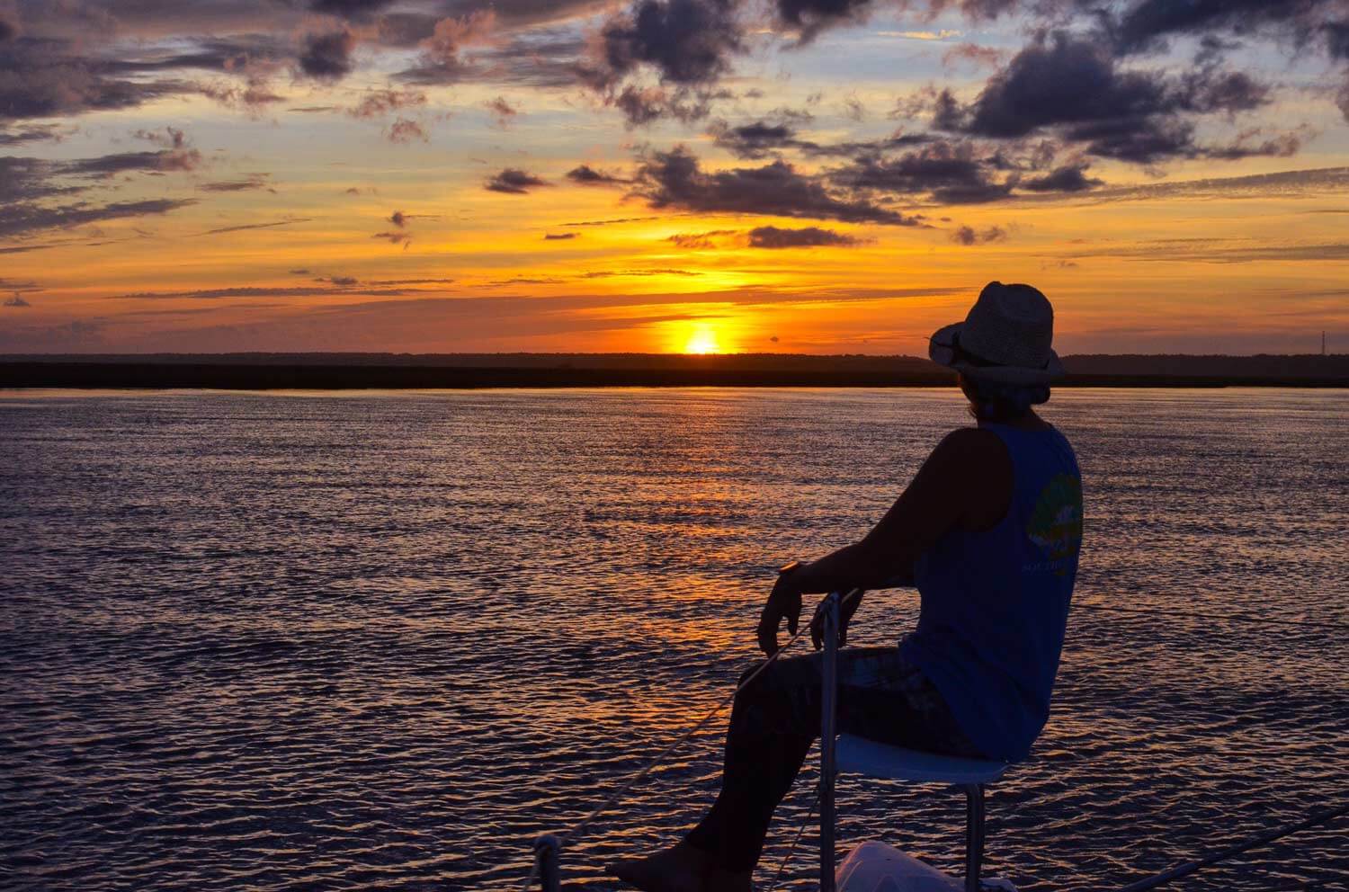 Person sitting on the bow of a boat looking out over the water at a sunset