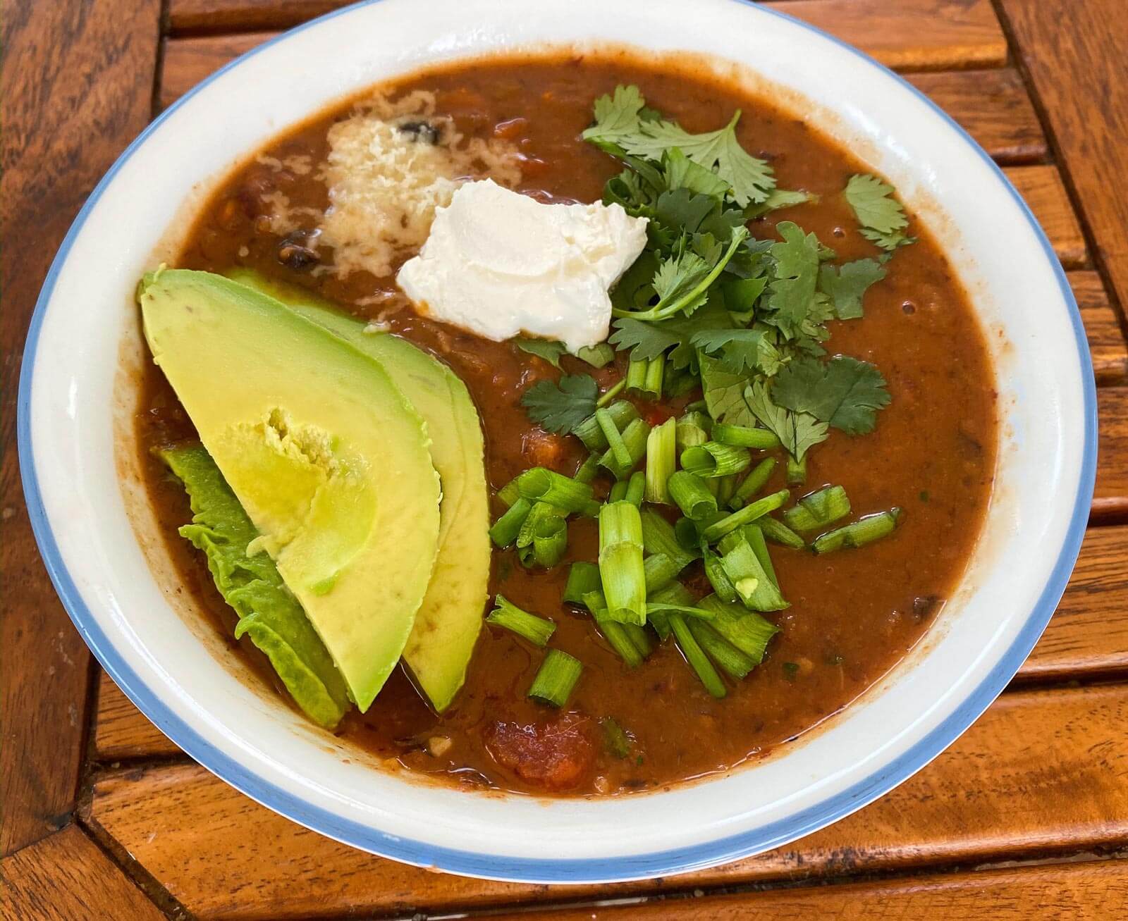 vegetable chili bowl with avocado, herbs, cheese, and sour cream as toppings