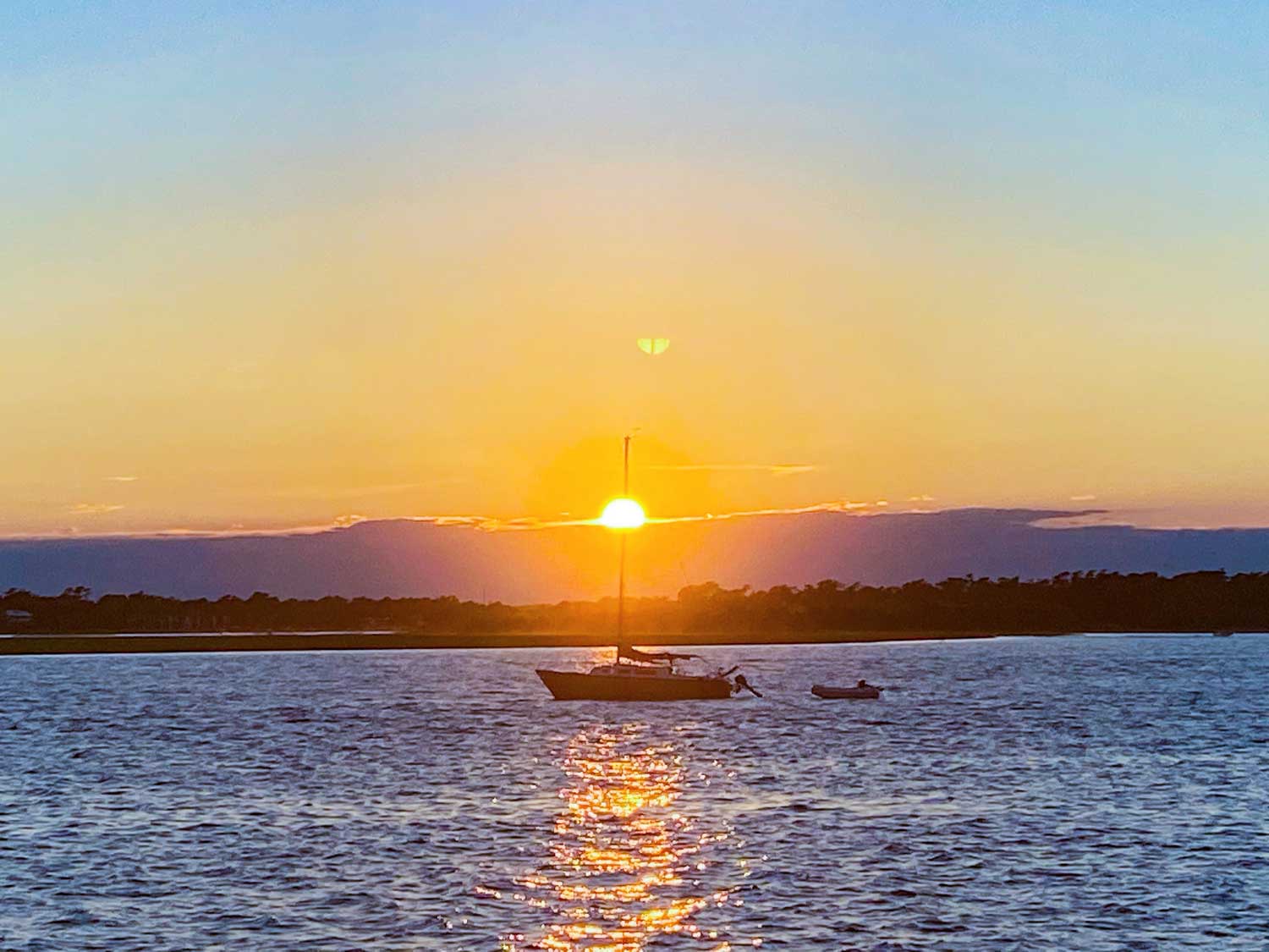 Sailboat at anchor with dinghy behind it at sunset