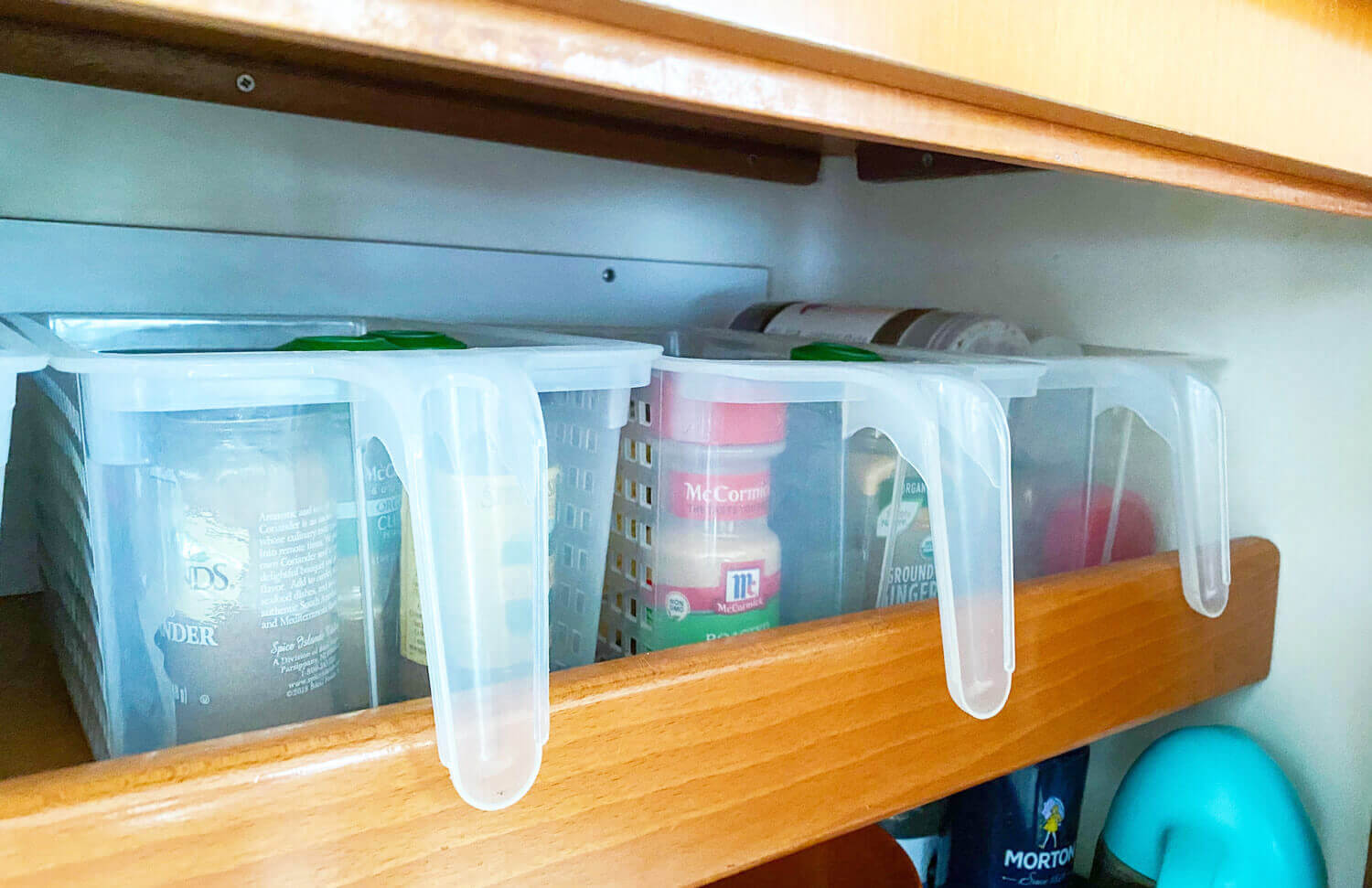 storage baskets with handles filled with spices and condiments sitting on shelf in boat galley cabinet