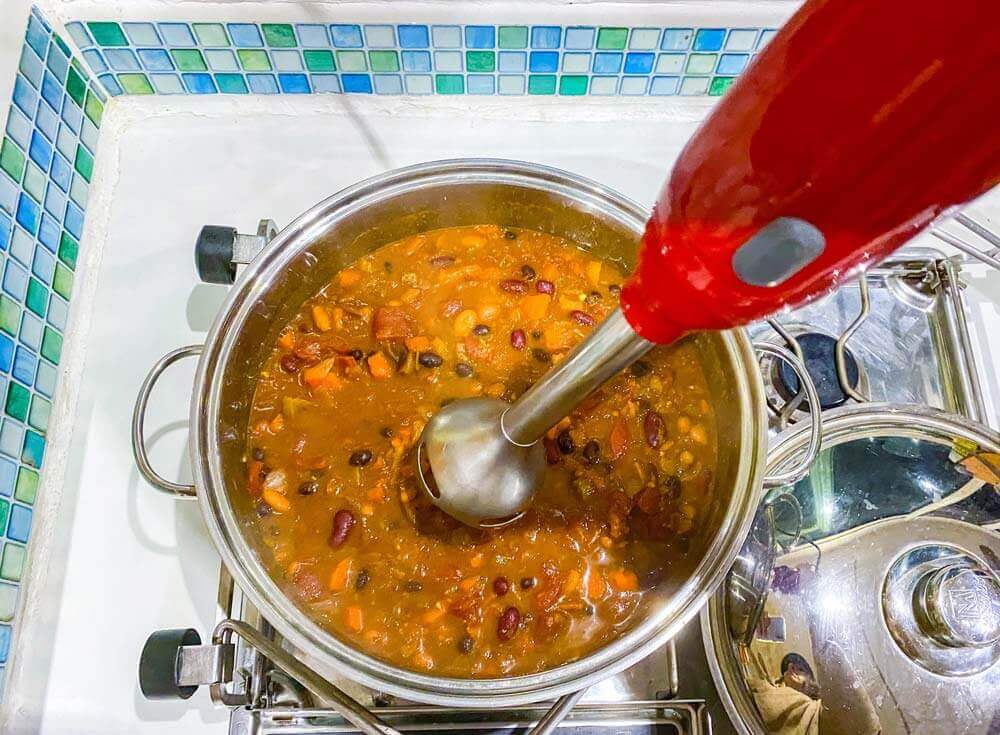 stick blender blending chili in large pot on stove