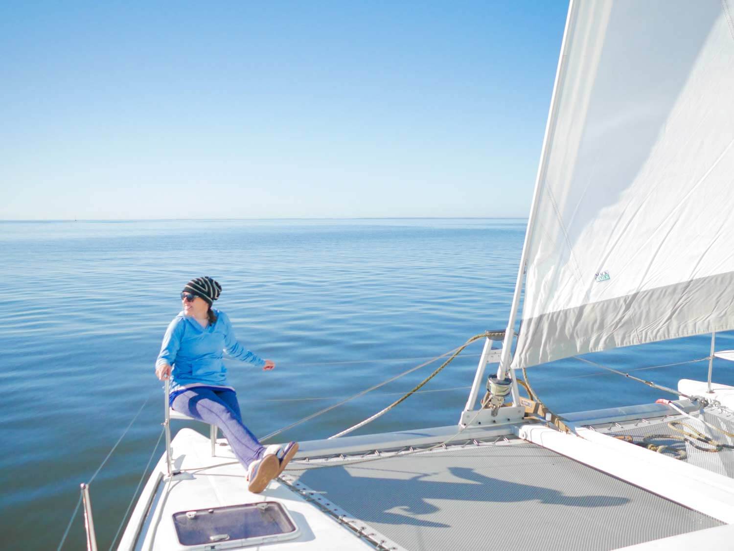 Crew member sitting on bow of sailboat under sail