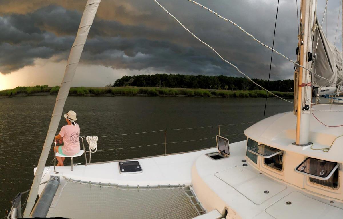 Sailing catamaran on anchor with storm clouds in the background.