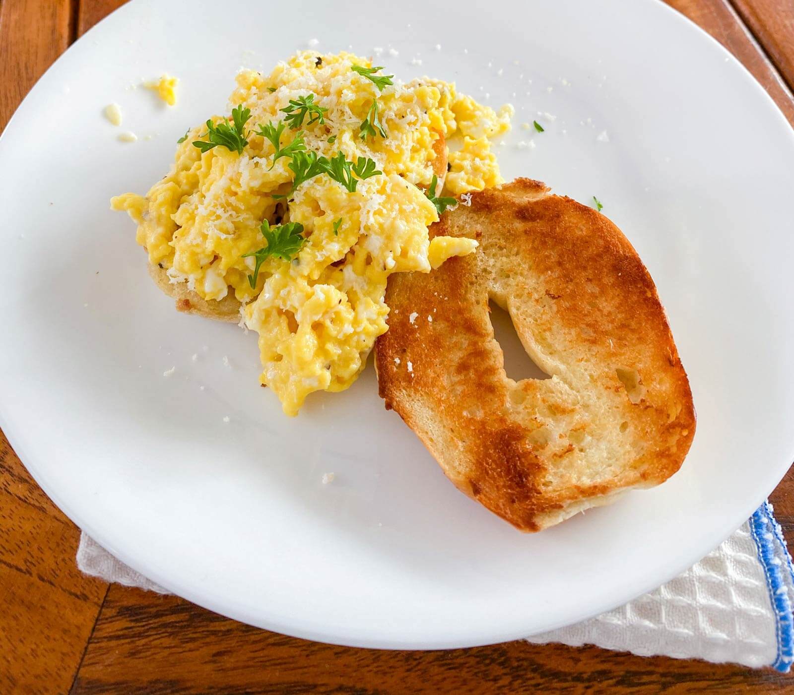 mini bagel and scrambled eggs topped with cheese and parsley on a white plate