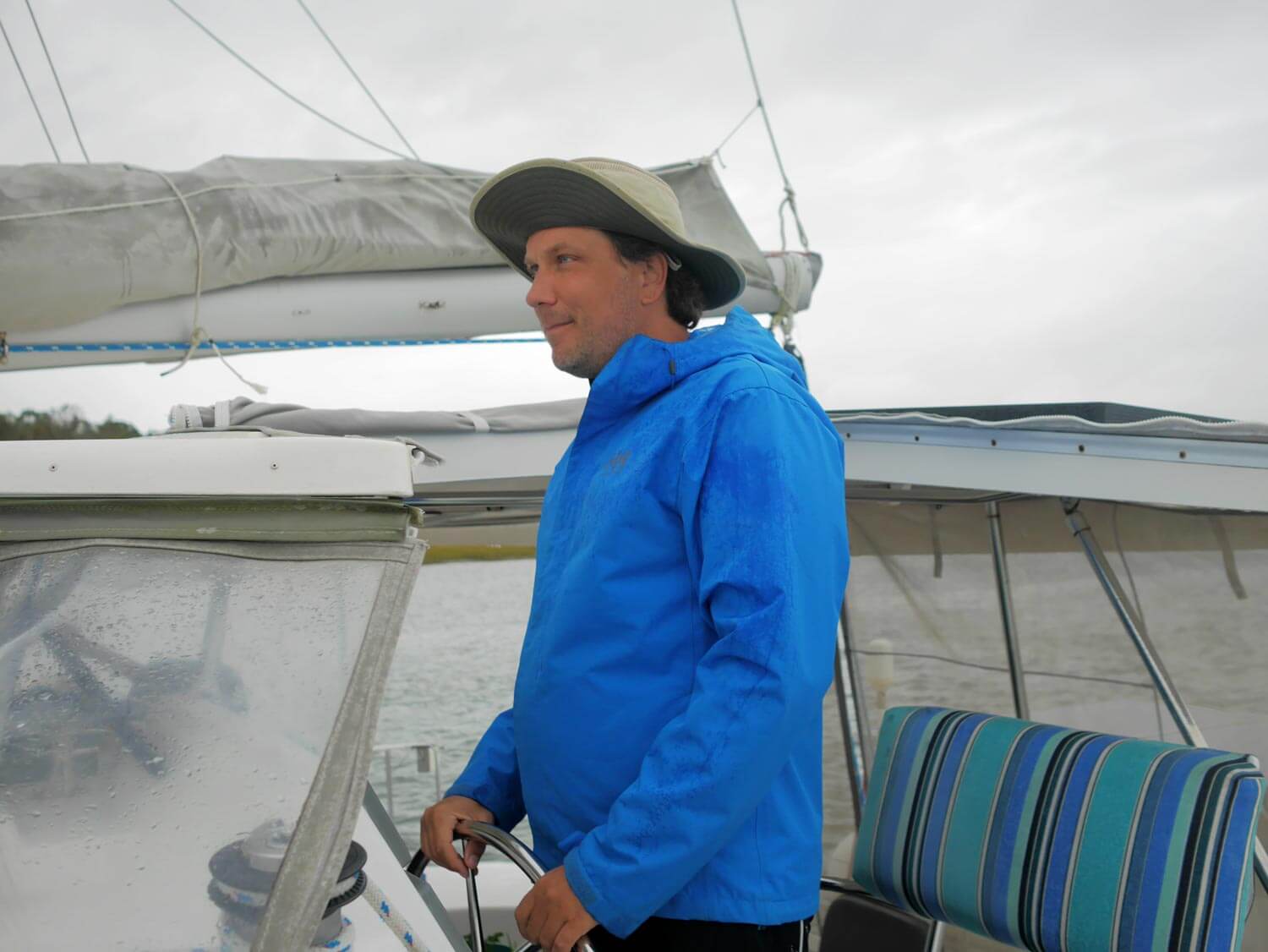 Man at helm wearing lightweight rain jacket and waterproof hat.