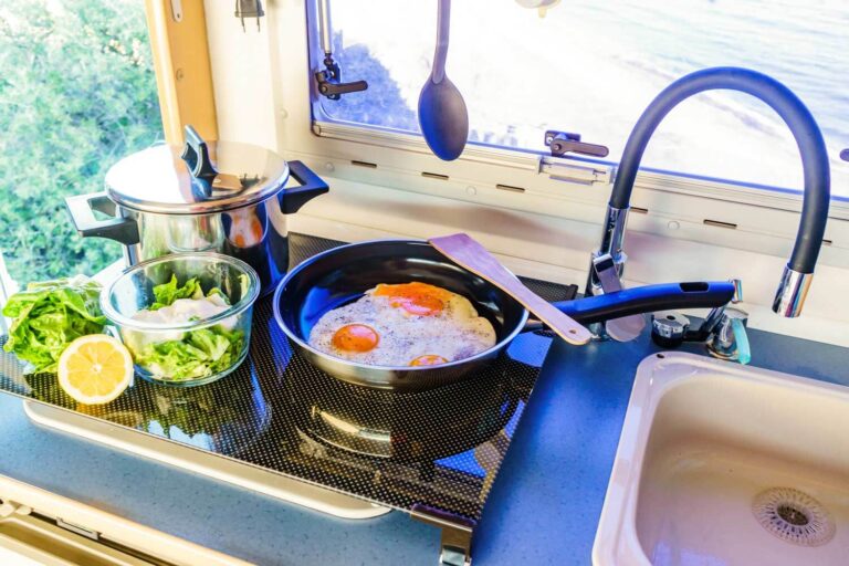 RV kitchen sink and stove with kitchen accessories and prepped food on the stove top