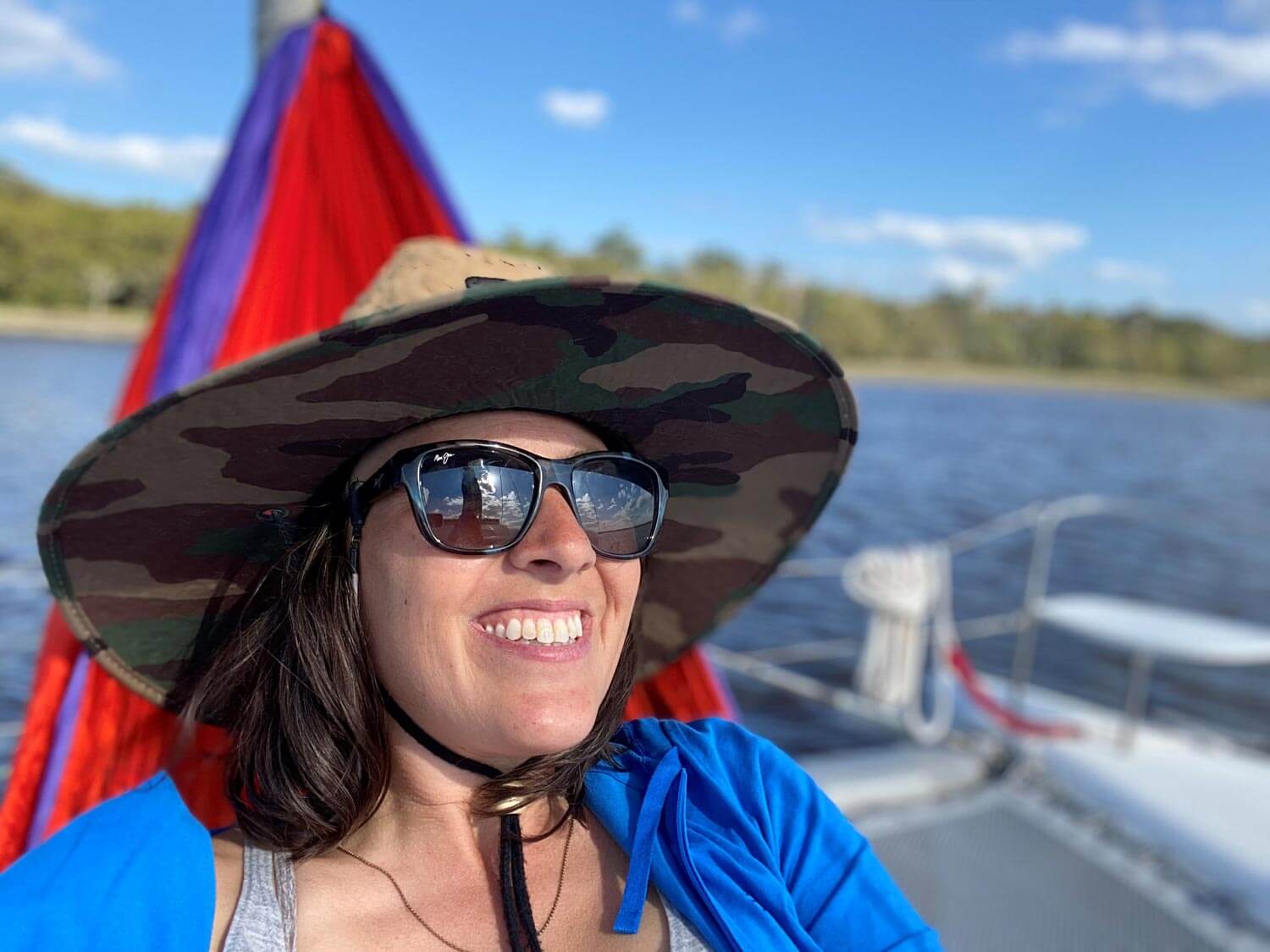 Woman in hammock on boat bow wearing large wide brim hat.