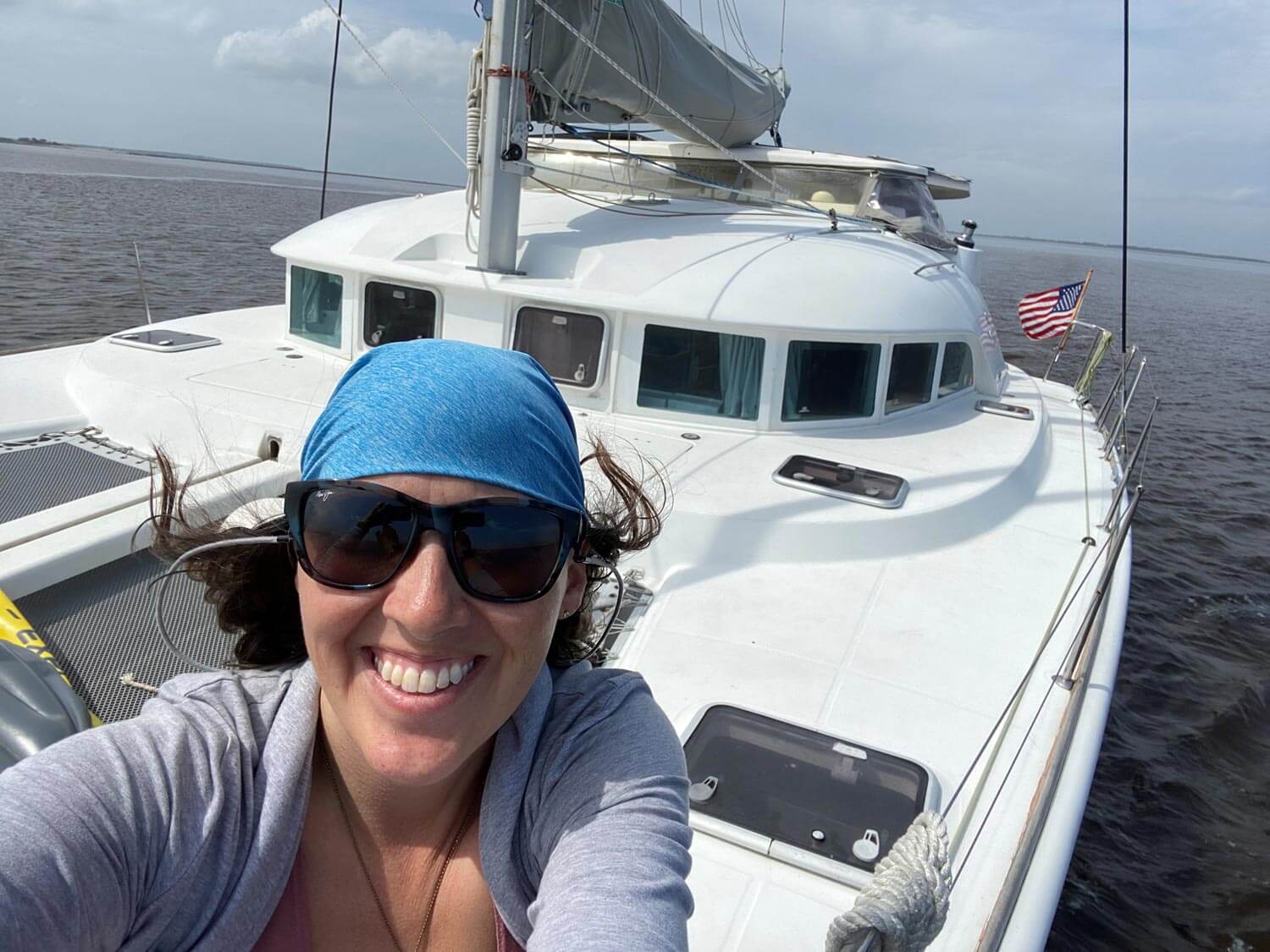 Woman on the bow of catamaran taking a selfie with bandana and sunglasses on.