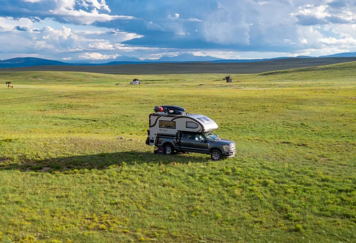 RV truck camper setup in a field with mountains in the background.