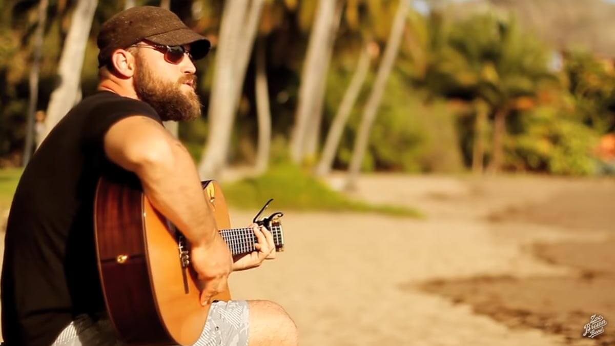 Zac Brown on a beach playing the guitar in his music video for the song Knee Deep.