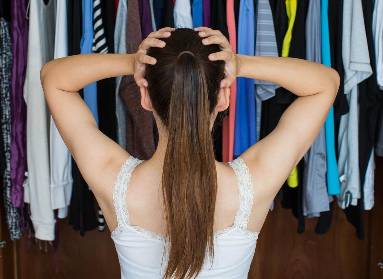 Woman standing in front of a closet with hands on her head.