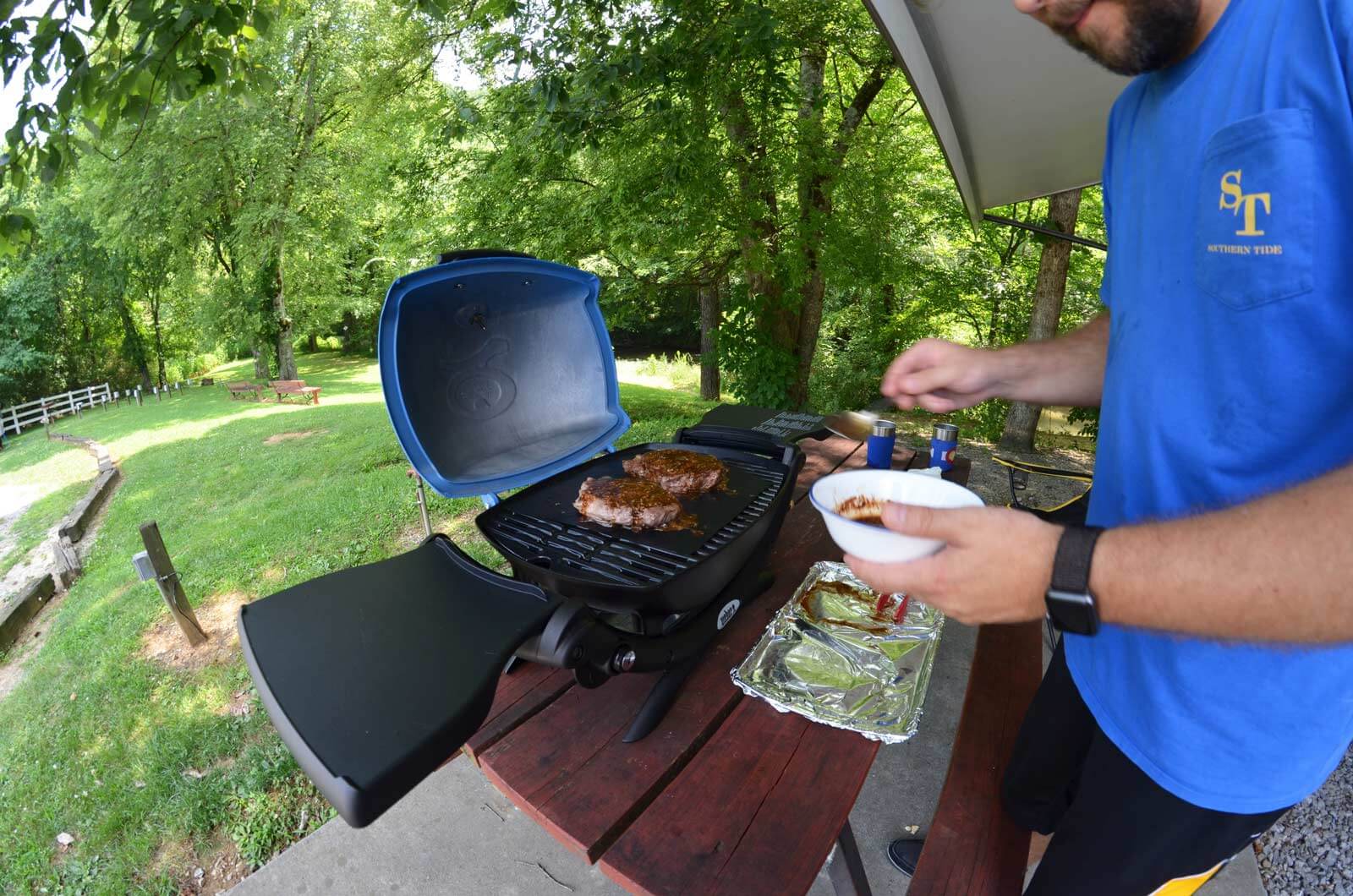 RVer cooking burgers on a weber grill at campsite.