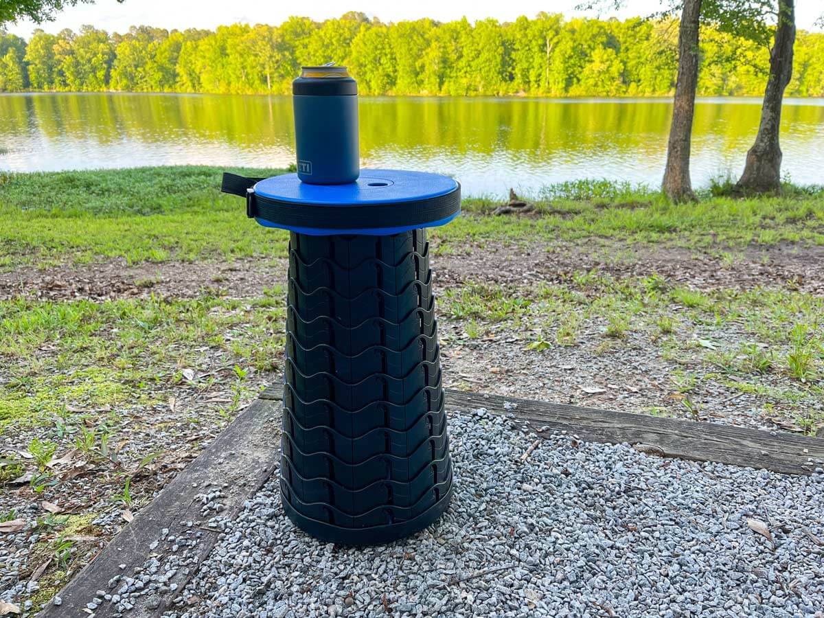 Retractable stool with beverage on top at a campsite.