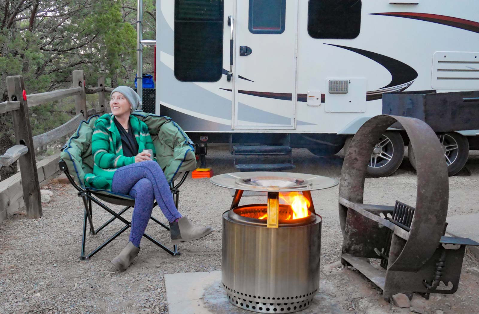 Woman sitting at an RV campsite with solo stove fire pit burning.
