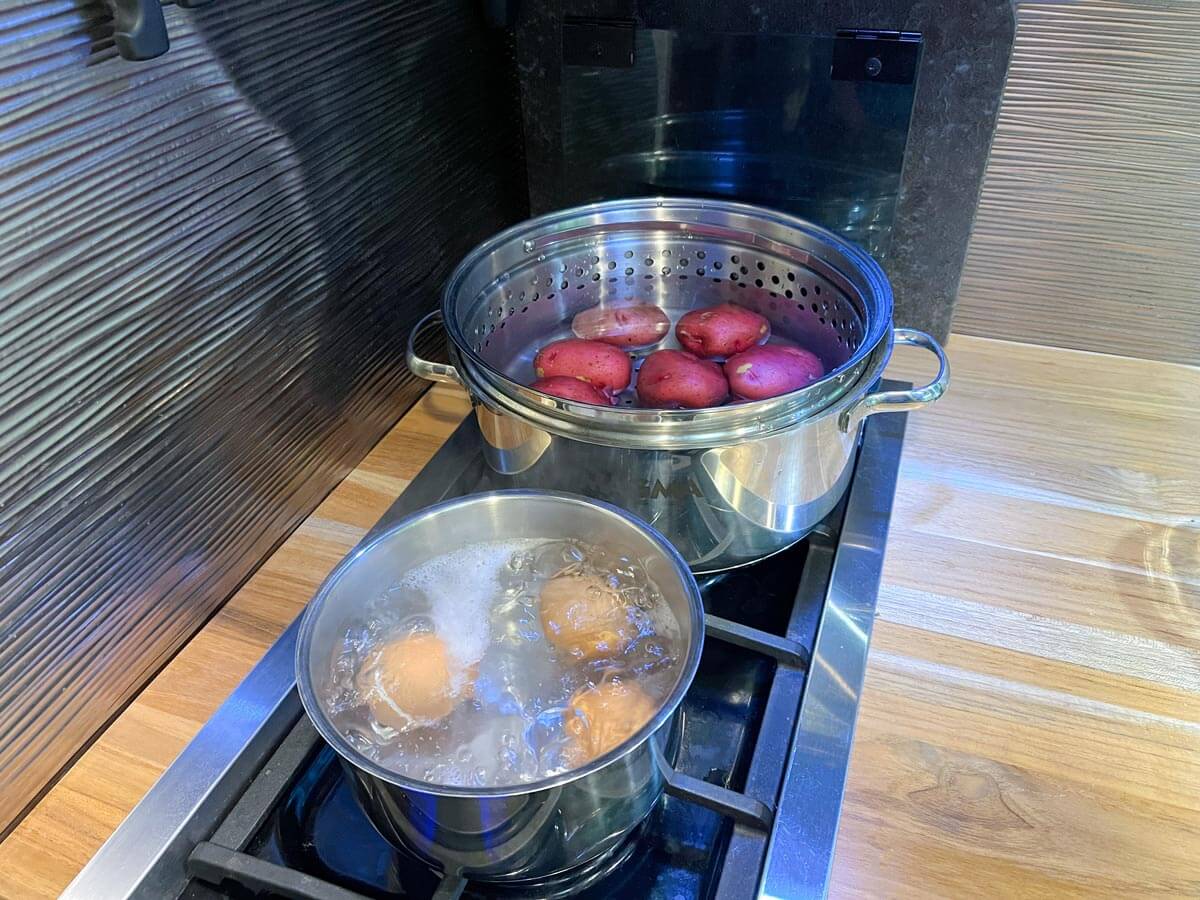 Magma large pot with strainer insert and small pot on stove with boiling potatoes and boiling eggs.