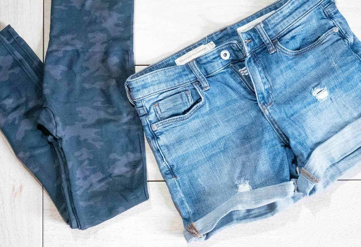Denim shorts with rolled cuff and camo leggings folded on table.