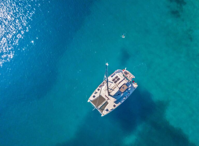 Ariel view of sailing catamaran in blue water with swimmer beside it