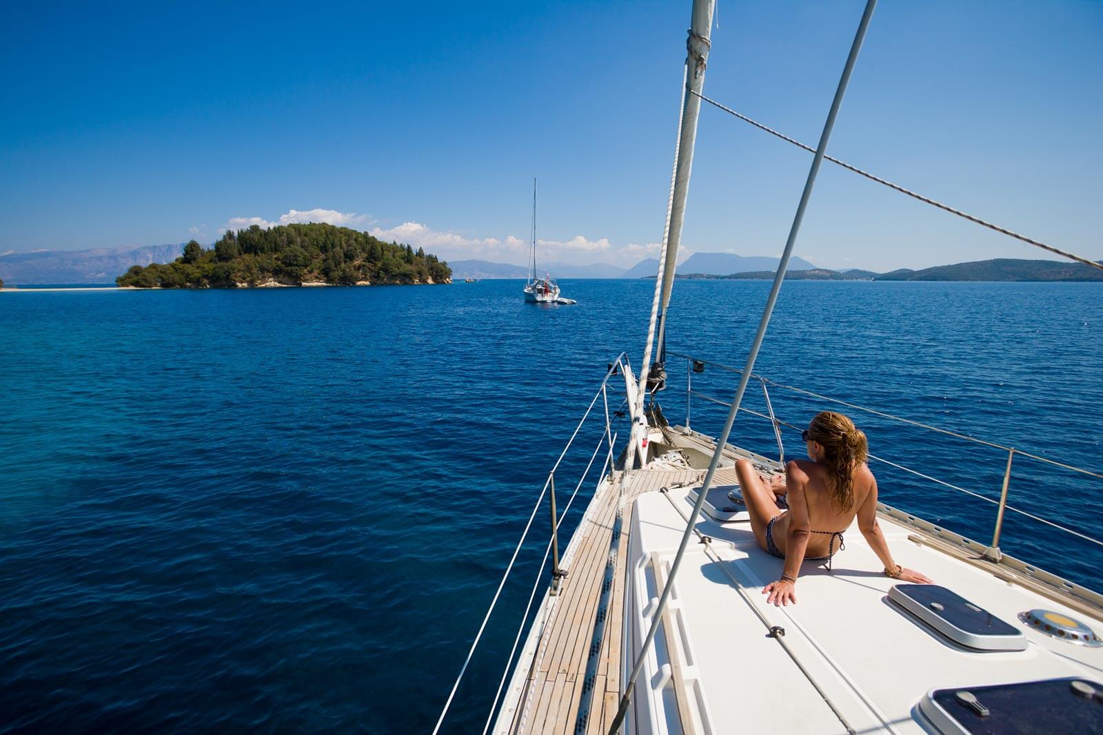 girl relaxing on the bow of a sailboat anchored in the water featured for best sailing Instagram accounts