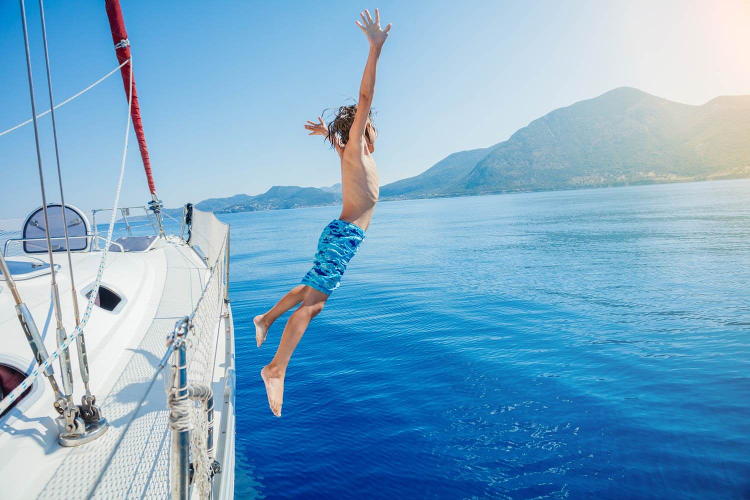 kid jumping off the side of a sailboat next to an island