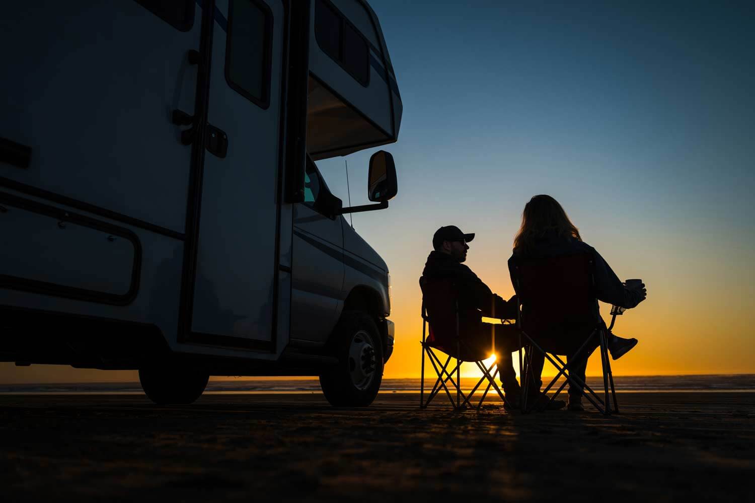 couple sitting in camping chairs in front of motorhome in remote location at twilight