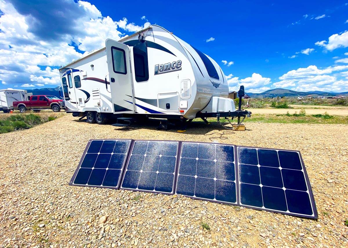 Portable solar panel setup in front of a travel trailer at a dry camping site.