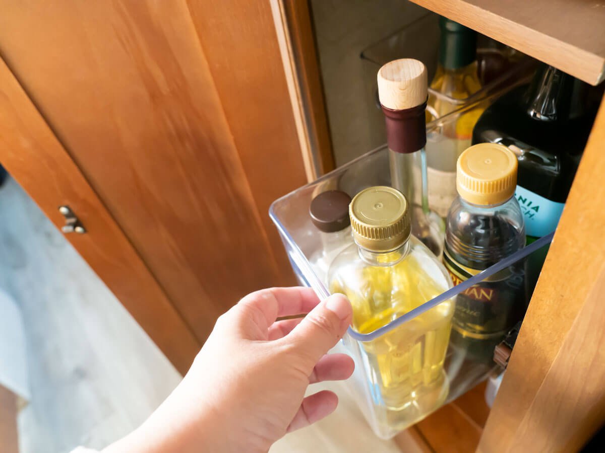 Woman pulling vertical bin out of narrow RV pantry with oil and vinegar bottles inside.