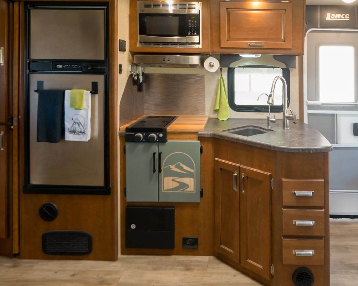 RV kitchen with fridge, microwave, stove top, sink, and many cabinets and drawers.