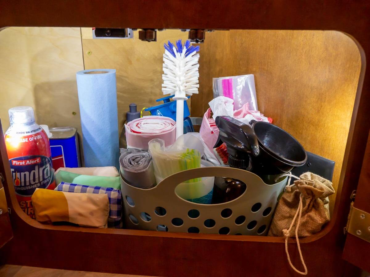 under the sink storage in an RV with basket full of bags, and other misc. kitchen items