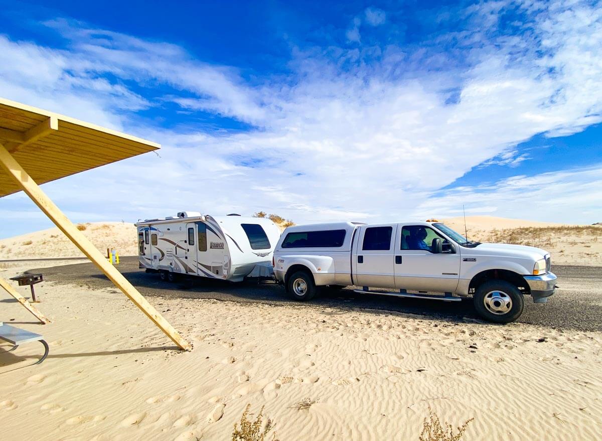 dually truck with camper shell and bumper pull travel trailer in sand dunes state park