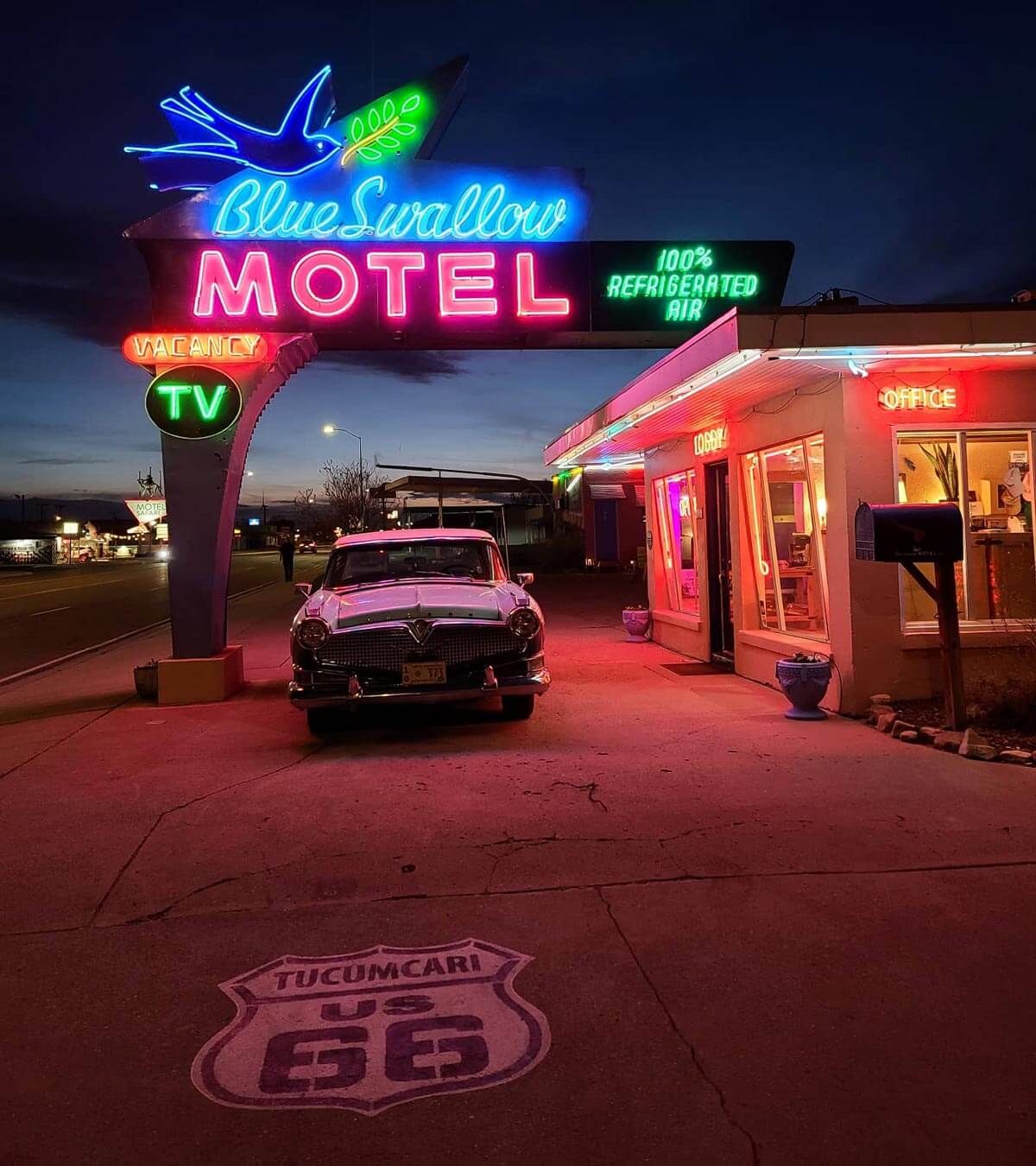 Blue Swallow Motel neon sign at night with old car out front and route 66 sign on the pavement.