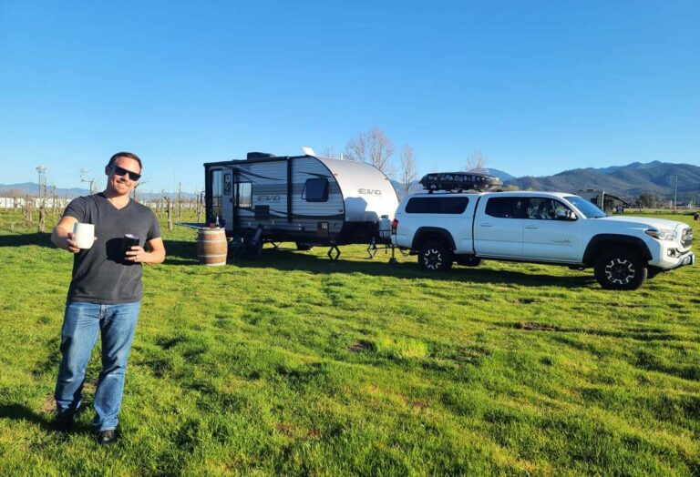 RVer holding wine with travel trailer setup in the background at a winery.