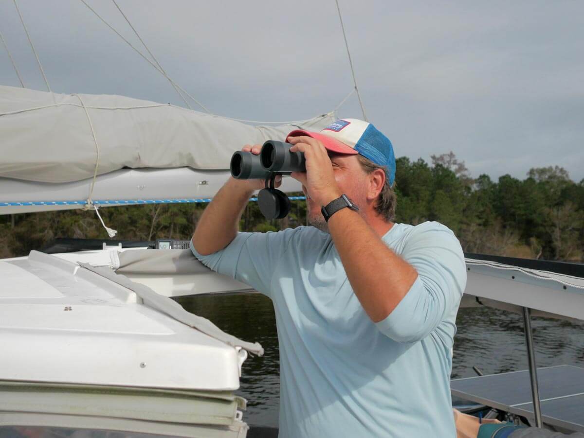 Sailor on sailboat using marine binoculars at the helm.