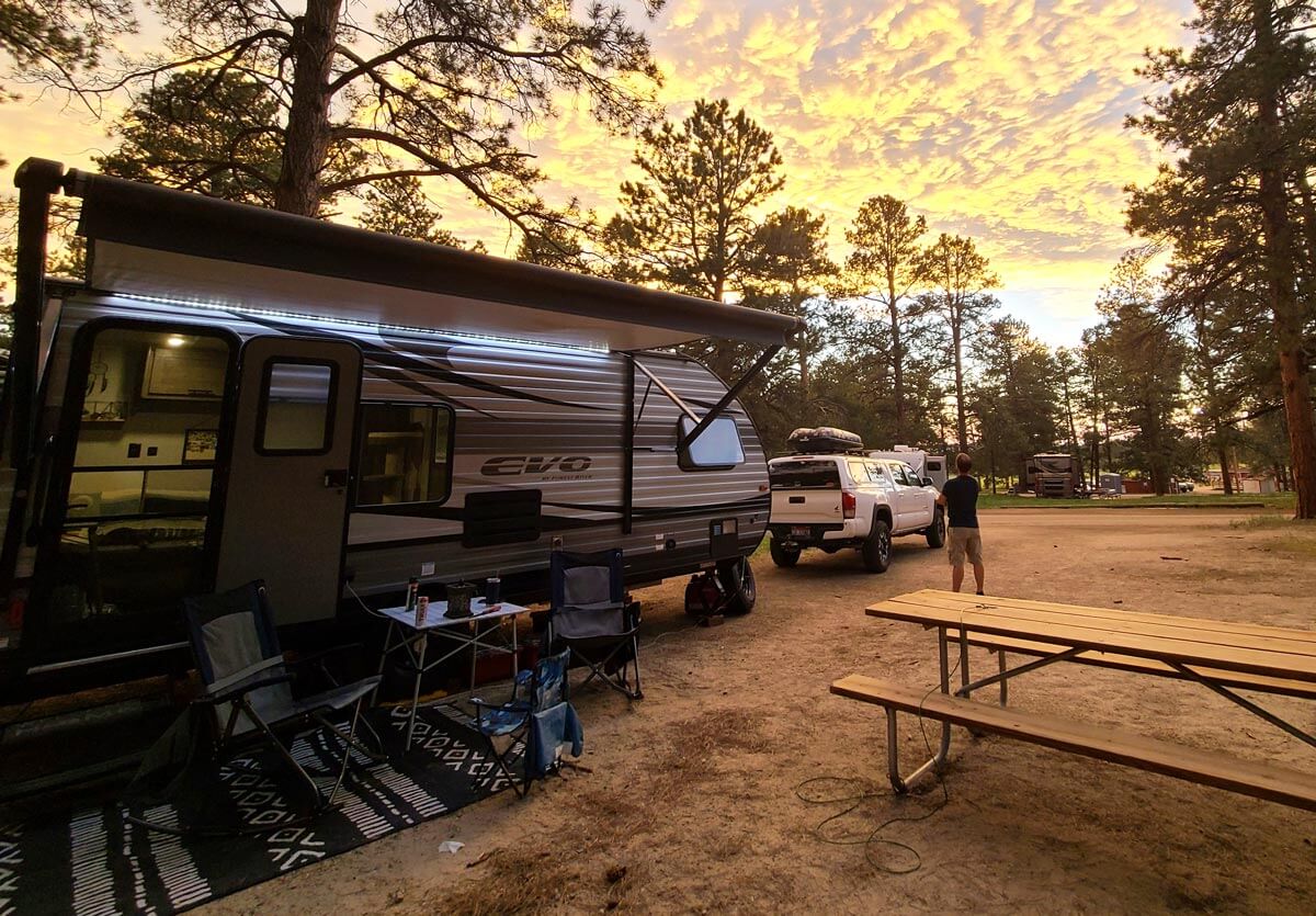 RV setup at campsite at sunset with chairs and table out front.