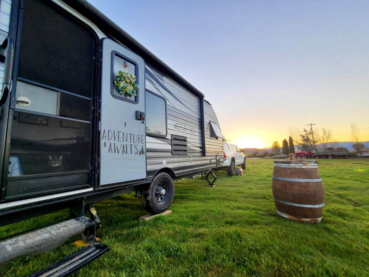 Travel trailer at sunset on a Harvests Hosts property parked in the grass with a wine barrel in front.