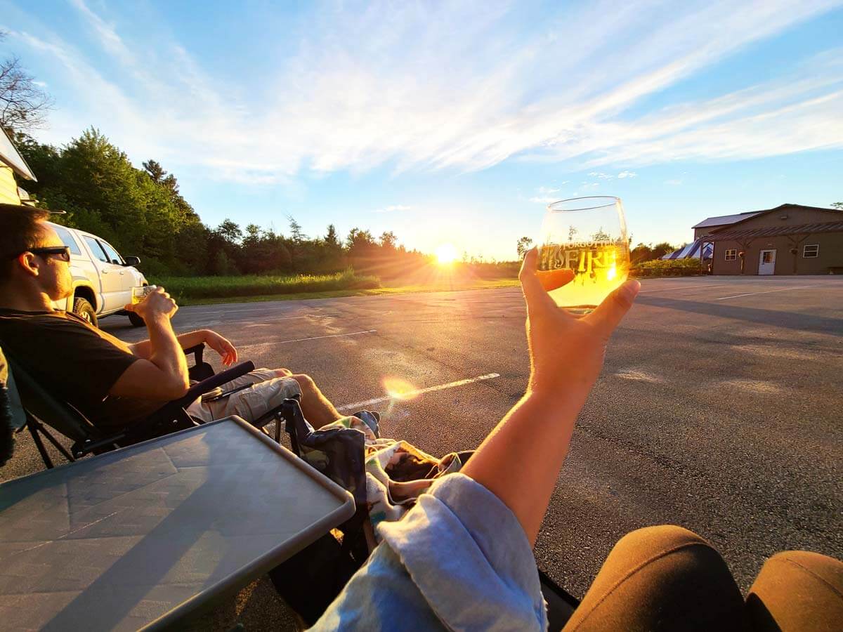 RVers raising a wine glass to cheers at a Harvest Hosts location with the sunset in the background.