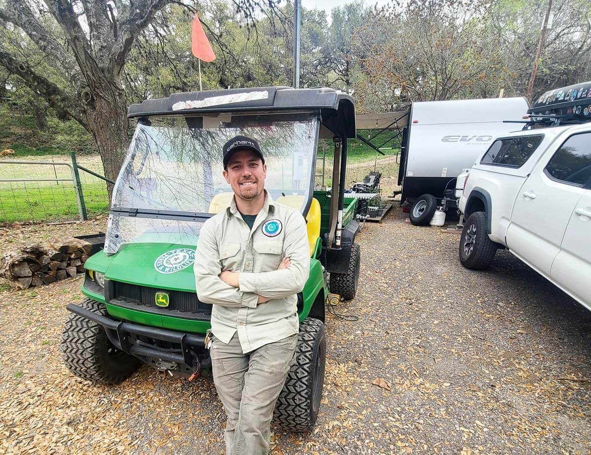 Workamper in uniform at campsite leaning on campground golf cart.