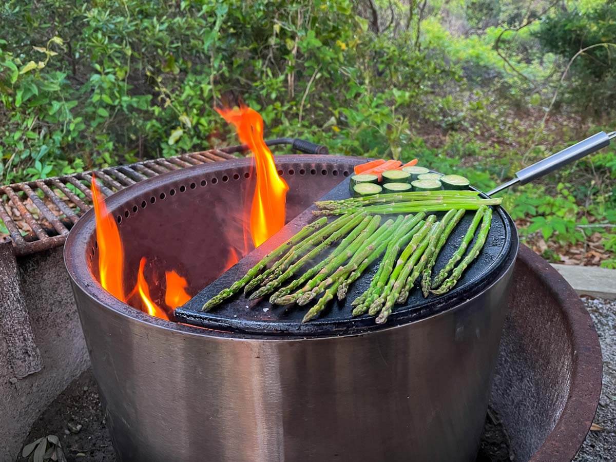 Vegetables cooking on a cast iron griddle on a Solo Stove fire pit.