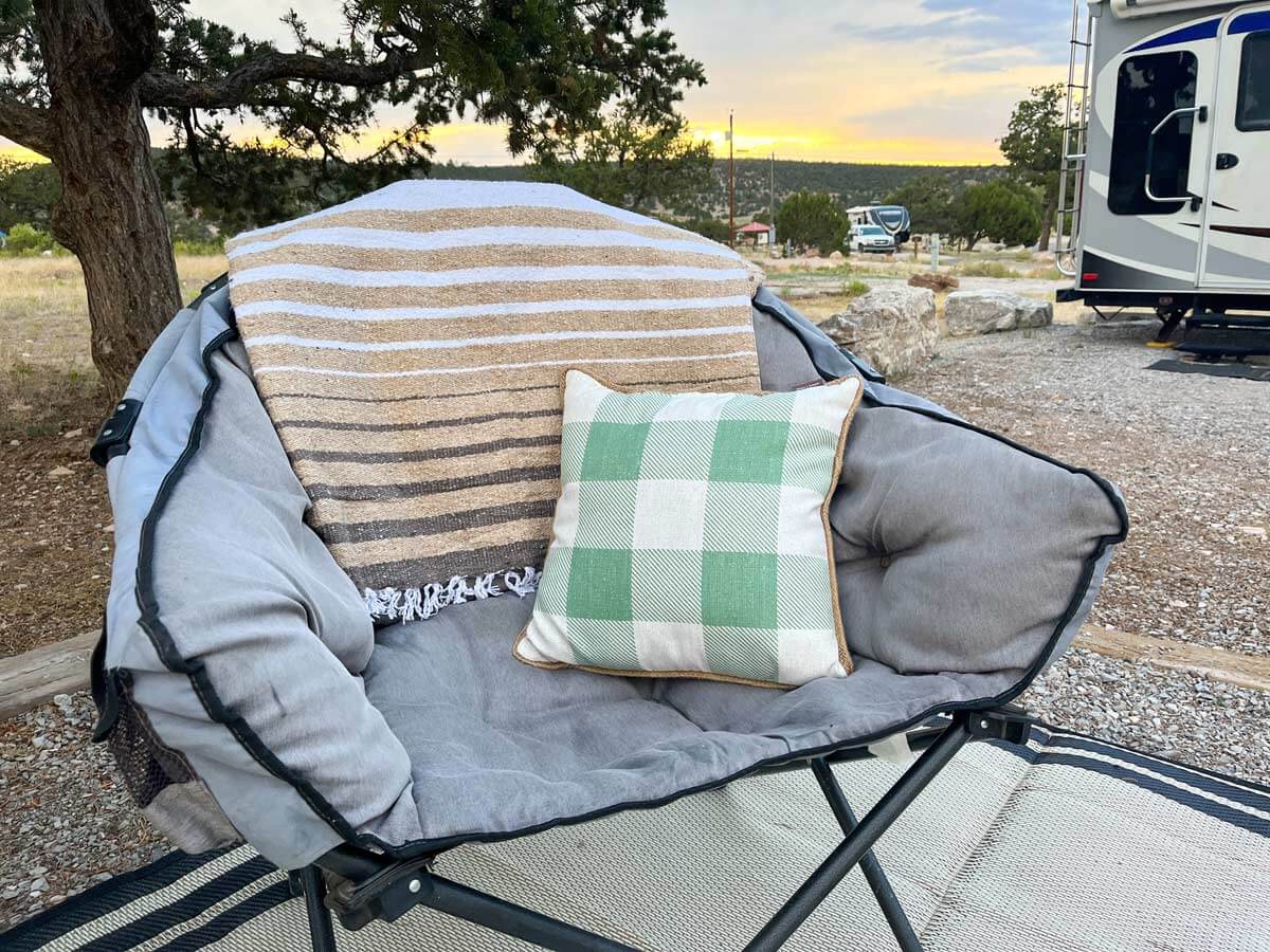 Camping chair with neutral color Mexican blanket tossed over the back and outdoor pillow in seat.