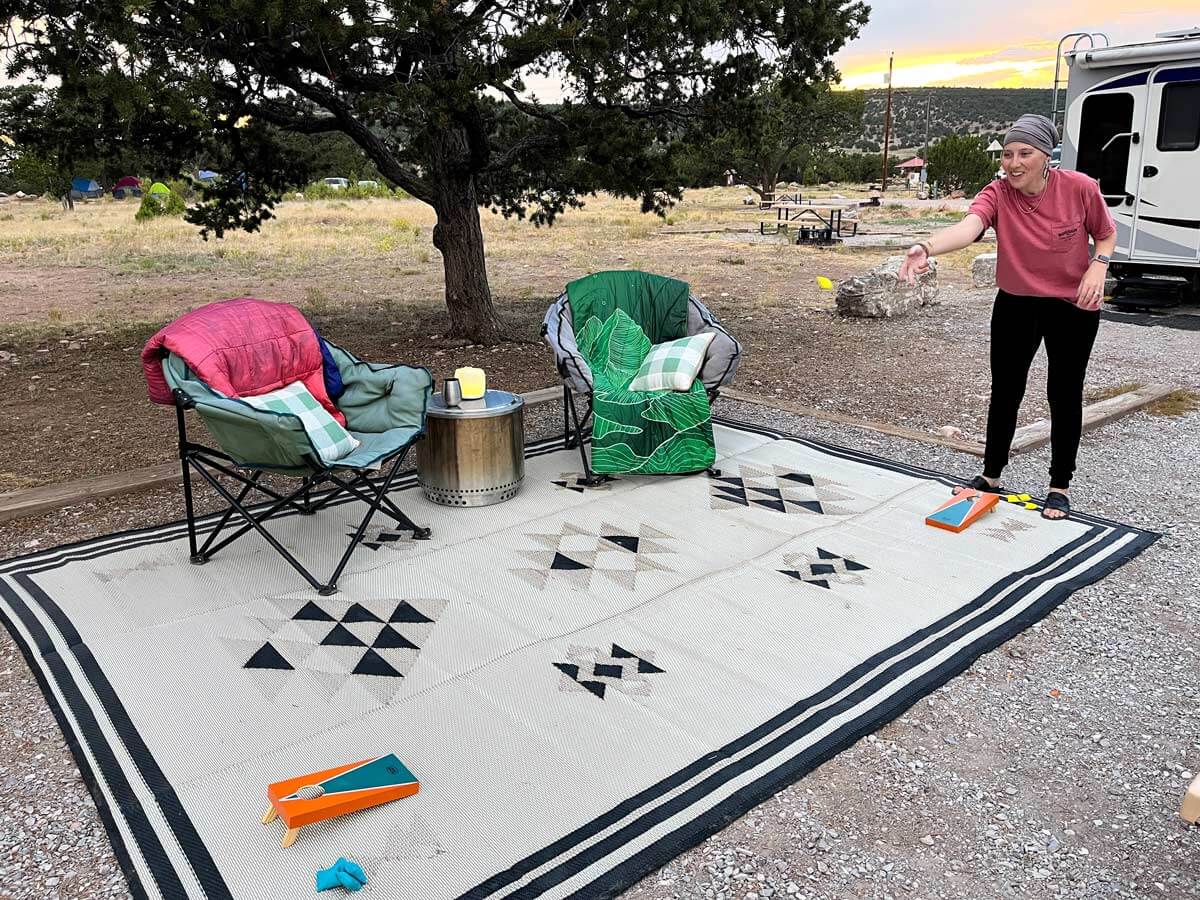 Woman playing cornhole with a miniature cornhole set in an RV campsite.