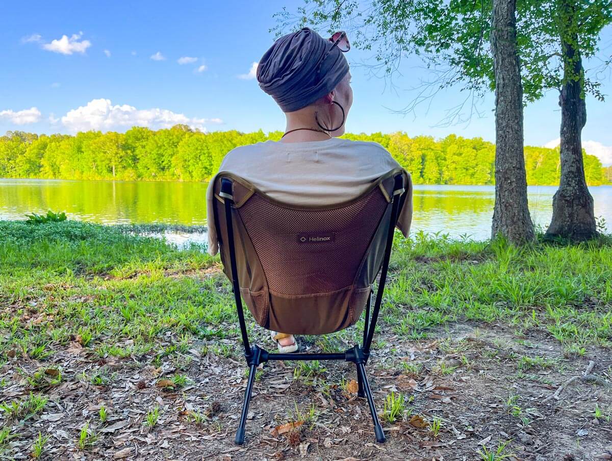 Woman in small camping chair in front of the lake.