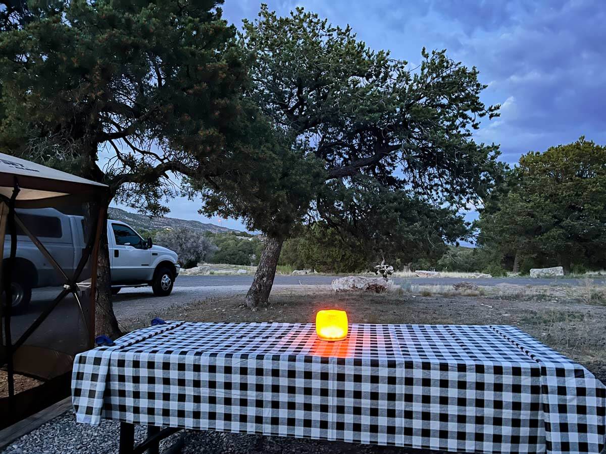 Picnic table at a campsite with black and white buffalo plaid table cloth and solar light in the middle.