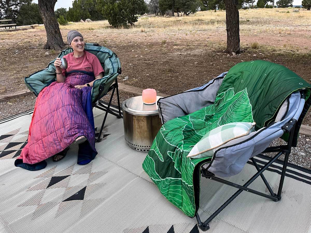 Woman wrapped up in Rumpl Nanoloft blanket with Rumpl Original Puffy in a chair beside her.