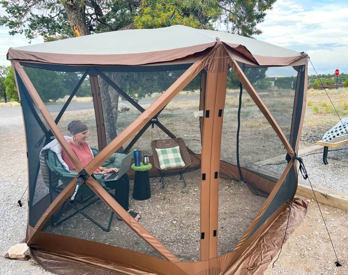 Woman working on computer inside a CLAM popup Gazebo in an RV campsite.