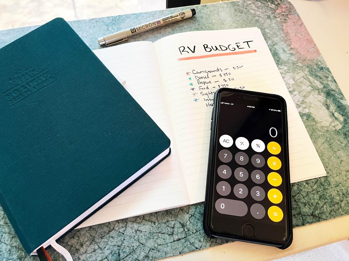 Notebook with "RV Budget" written in the headline and various categories of expenses underneath and the calculator app open on an iPhone.