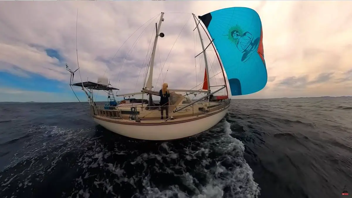 Screenshot of Sailing SV Delos YouTube video showing a wide shot of the Delos vessel from the side and Karin on the beam of the boat.